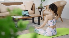 Asian woman doing yoga indoors while looking at a computer.