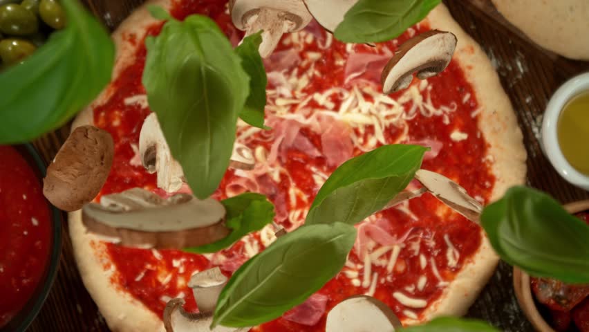 Super slow motion of falling basil leaves and mushrooms on pizza dough with camera follow and rotation. Filmed on high speed cinema camera, 1000 fps.