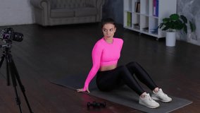 Athletic woman in sports wear having workout at home while lying on the mat and doing exercises, recording on a camera on a tripod. Home fitness, workout concept. Real time video.