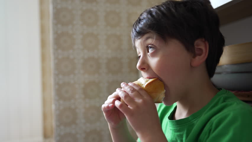 Five-year-old boy captured up-close enjoying a piece of bread, emphasizing a child's simple pleasure in snacking Royalty-Free Stock Footage #3496264613