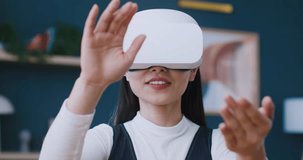 Camera view of woman wearing virtual reality headset at home. Moving hands in imaginary world. Exploring virtual objects with 3D glasses. Girl getting excited while looking at digital image.