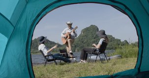 Happy family backpacker playing guitar and singing  while having camping near lake. 4k video