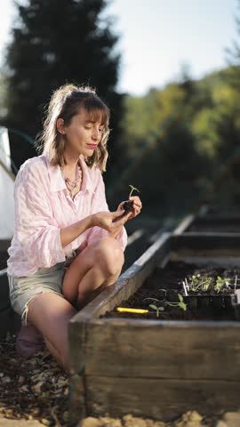 Young woman plants vegetable sprouts at her backyard garden. Growing organic food near home