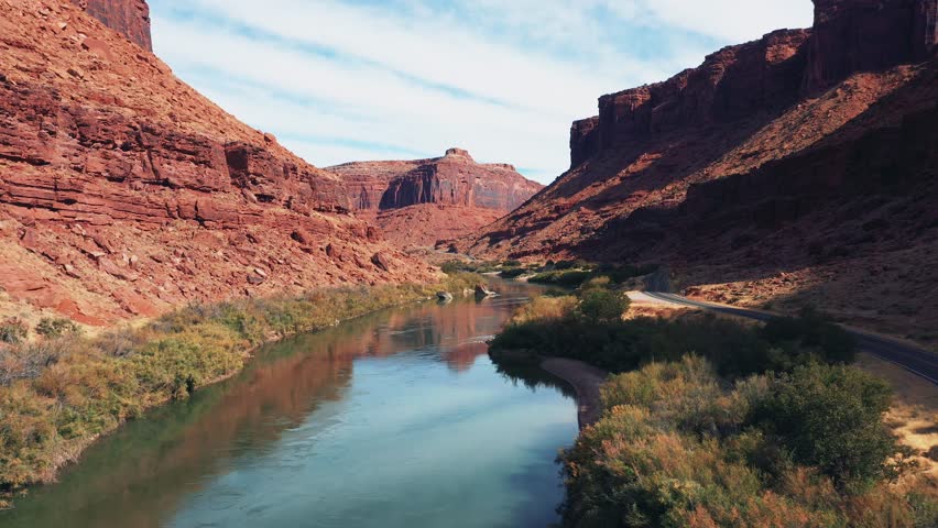 Drone flies over Colorado river, flows from red rock massif of brick structure in canyon is destroyed by soil erosion and precipitation. Travel In western Usa in Utah state, curve highway along shore