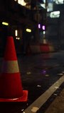 A bright neon traffic cone sits on the side of a road in a quiet Asian city during a rainy night.