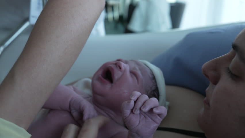 Newborn baby first cries after birth, authentic real life childbirth moment of human being crying for the first time having left mother's womb resting on mom's chest, skin to skin