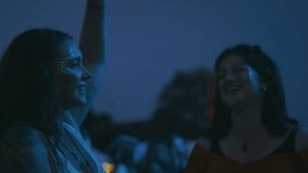 Two female friends wearing glitter holding drinks having fun dancing at outdoor summer music festival at night - shot in slow motion - Powered by Shutterstock - Get 15% off with code: PIKWIZARD15