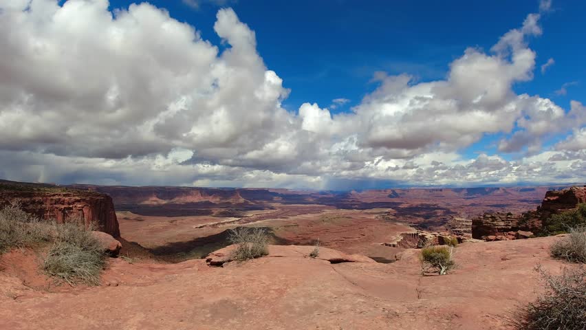A timelapse of clouds over Canyonlands National Park in southern Utah. Stratus clouds are moving overhead from behind while camera pans left to right. Royalty-Free Stock Footage #3496518249