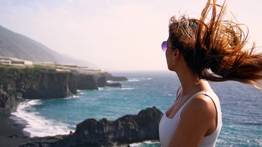 a woman relaxing on the top of a cliff with her hair blown by the wind in slow motion, in La Palma, Canary Islands