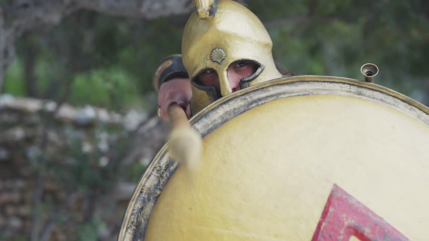 Spartan hoplite warrior going forward in attack with spear and protecting with shield at Acropolis in Athens, Greece, cinematic slow motion shot