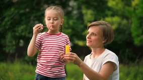 Mother and little girl find delight in shared activity of blowing soap bubbles. Park becomes place of joy as mother and daughter blow bubbles together. Mom and daughter blow bubbles slow motion - Powered by Shutterstock - Get 15% off with code: PIKWIZARD15