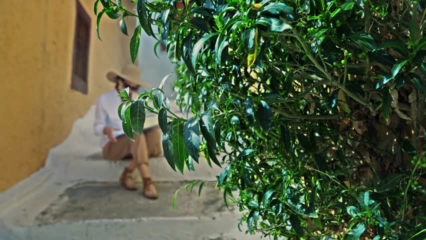 Woman with hat looking at map sitting on staircase of Anafiotika, a part of old historical neighborhood Plaka on northern-east side of the Acropolis hill, Athens, Greece.