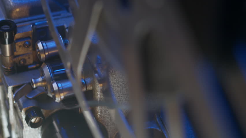 A close-up shot captures the vintage charm of a 16mm film projector's reels under a soft blue glow. The projector plays a classic film on mid-20th century technology.