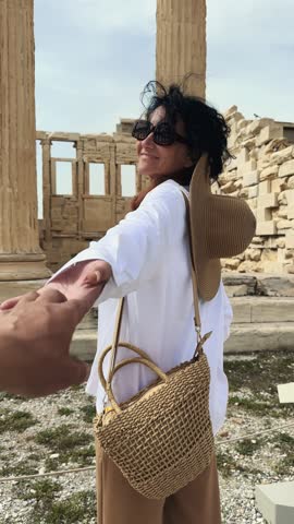 Young couple at honeymoon trip visiting ancient Acropolis in Athens, holding hands and smiling, pov, vertical orientation