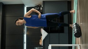 Young woman stretches in kitchen at home. Sporty fit female in athletic workout clothes doing stretching exercises. Girl doing morning fitness. Vertical video
