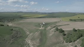 Aerial flat video. Fairytale place with fluffy clouds and hills full of green trees and rapeseed. A flock of sheep and birds flying over the hills and in the distance country roads and a few houses
