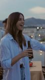 Vertical slow motion video of happy woman dancing with friends at summer party on rooftop terrace. Millennial people enjoying funny moments together at weekend celebration.