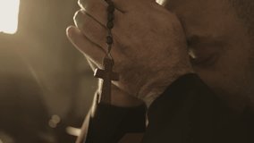 Christian monk holding rosary in clasped hands and praying with closed eyes close up. Beads with cross hanging from man clenched fists during prayer in church closeup - Powered by Shutterstock - Get 15% off with code: PIKWIZARD15
