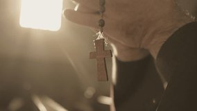 Christian rosary with cross hanging from male hands and swinging close up. Monk holding prayer beads in clasped arms while praying in cathedral closeup. Christianity concept - Powered by Shutterstock - Get 15% off with code: PIKWIZARD15