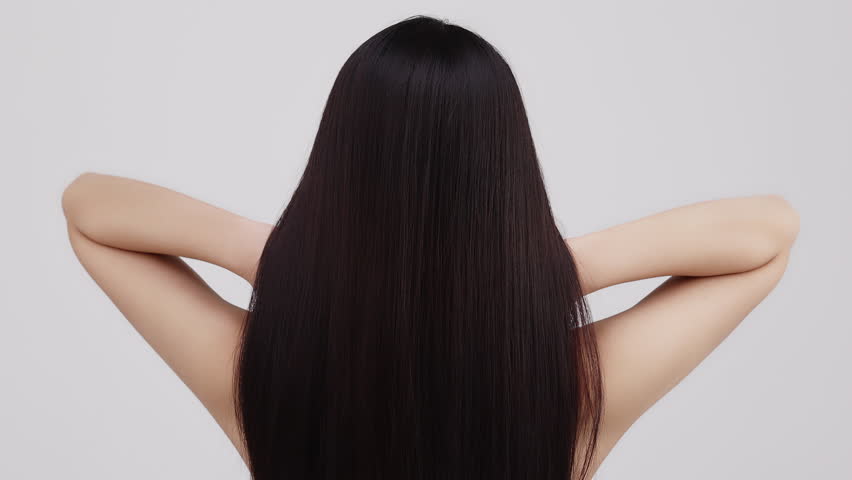 Slow motion rear view of young Asian girl shakes long straight hair. Female model is fluttering hair.