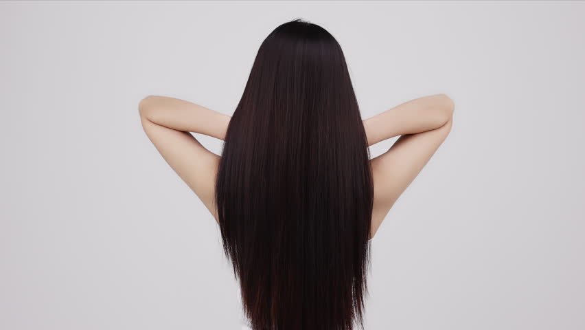 Slow motion rear view of young Asian girl shakes long straight hair. Female model is fluttering hair.