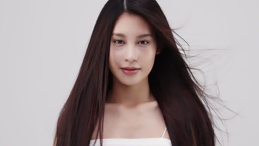 Slow motion close-up portrait of a smiling brunette woman with long hair that slowly blown by the wind.