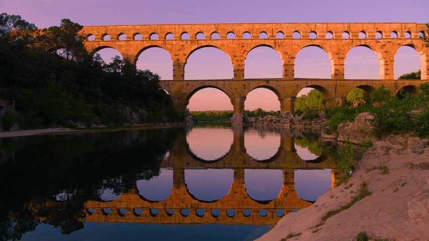 Spring Evening at Pont du Gard - A panoramic view of the famous Pont du Gard, an ancient roman aqueduct bridge, reflecting in calm Gard River, on a colorful Spring evening. Nimes, southern France.