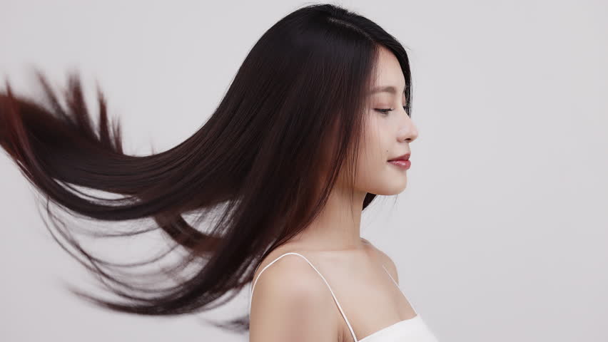 Slow motion close-up portrait of a smiling brunette woman with long hair that slowly blown by the wind.