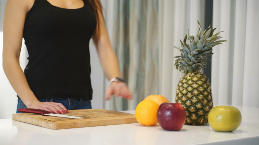 Female hands cutting orange on a wooden board. Woman in the kitchen. Healthy eating. Raw food.