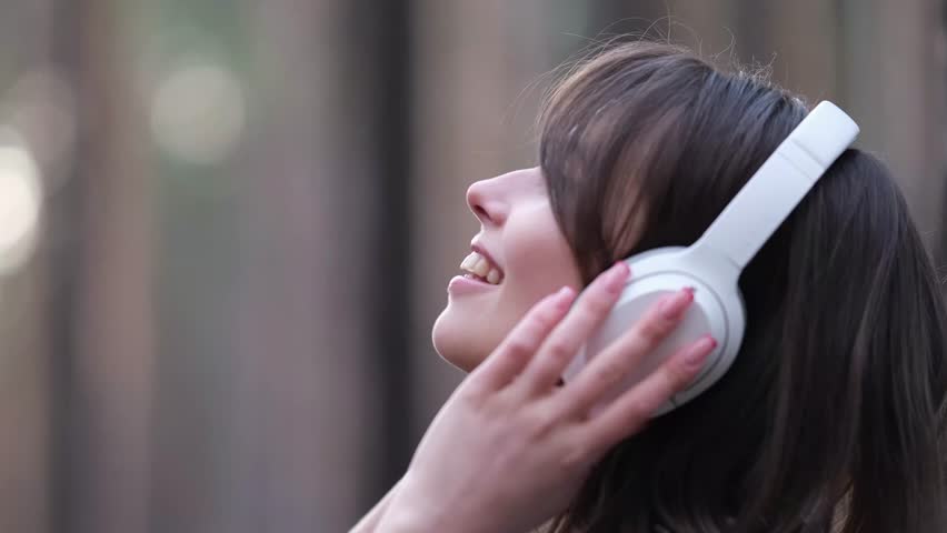Young beautiful brunette listens to music on headphones outdoors. A woman dances joyfully to music among the maidens in the forest.