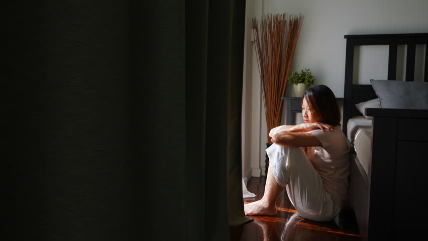 4K Depressed Asian woman sitting in bedroom and hugging herself with sadness. Loneliness sad woman living alone with negative emotion. People mental health and life problem concept.