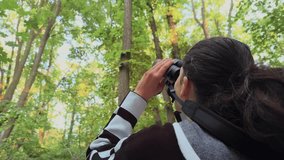 Birdwatching. 4K video with a woman filmed from behind while searching and scouting the forest canopy for birds with a binocular. - Powered by Shutterstock - Get 15% off with code: PIKWIZARD15