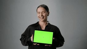 A beautiful young woman with a smile holds a tablet with a green screen. Placement of ads on the gadget - Powered by Shutterstock - Get 15% off with code: PIKWIZARD15