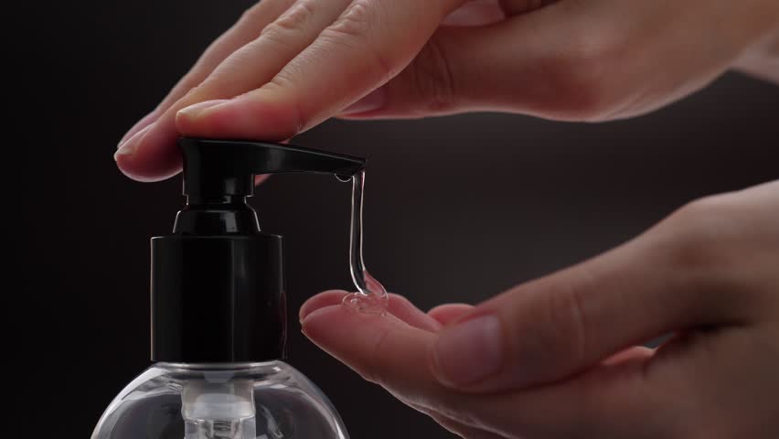 Woman push dispenser and liquid soap squeezed out to hand, closeup shot against black background. Lady washing up hands at bathroom, using soft gel for advanced skin care
