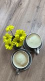 Two Cups of Cappuccino Coffee and Vase of Yellow Flowers
