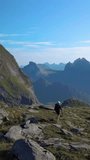 Aerial view of a girl with a backpack traveling through the mountains. Beautiful view of the peaked tops of the Lofoten Islands, Norway, vertical footage