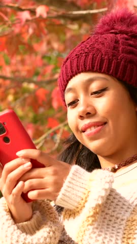 Portrait of an Asian woman in autumn with a mobile phone calling in a forest of red leaves, technology