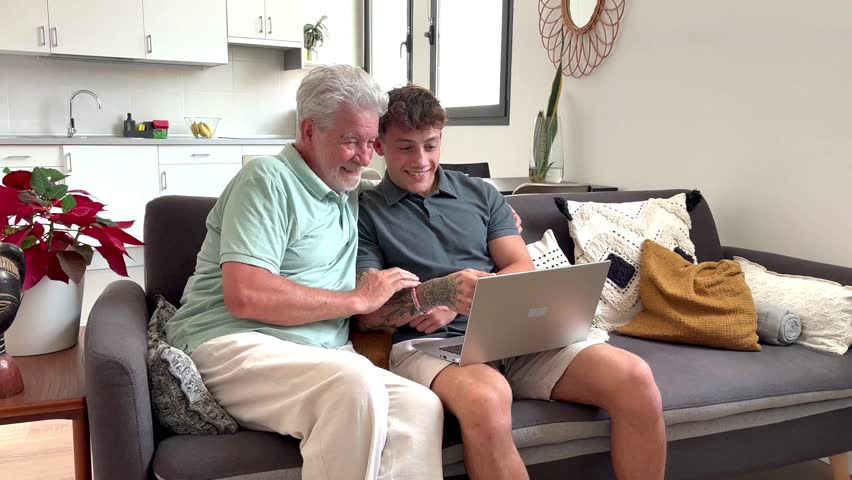 Senior man and young boy smiling and looking together at laptop at home. Smiling nephew teaching and showing new computer technology to his old grandfather. Old man learn how use computer.