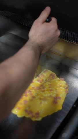 A cook frying the ham tortilla with cheese on the griddle in the kitchen of the bar or restaurant