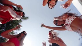 Women friends clink glasses with champagne and drink for good, fun summer holidays in country luxury club. Models in bright bikinis relaxing with alcohol and waving in camera. Shoot from below. - Powered by Shutterstock - Get 15% off with code: PIKWIZARD15