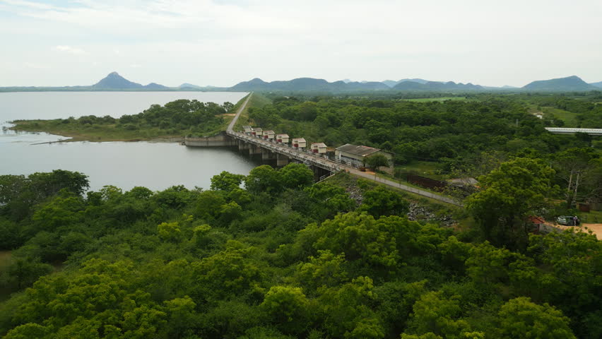 Aerial view captures Sri Lanka river dam surrounded by rich greenery, mountains in distance. Hydroelectric power generation, nature conservation, travel destination in drone shot.
