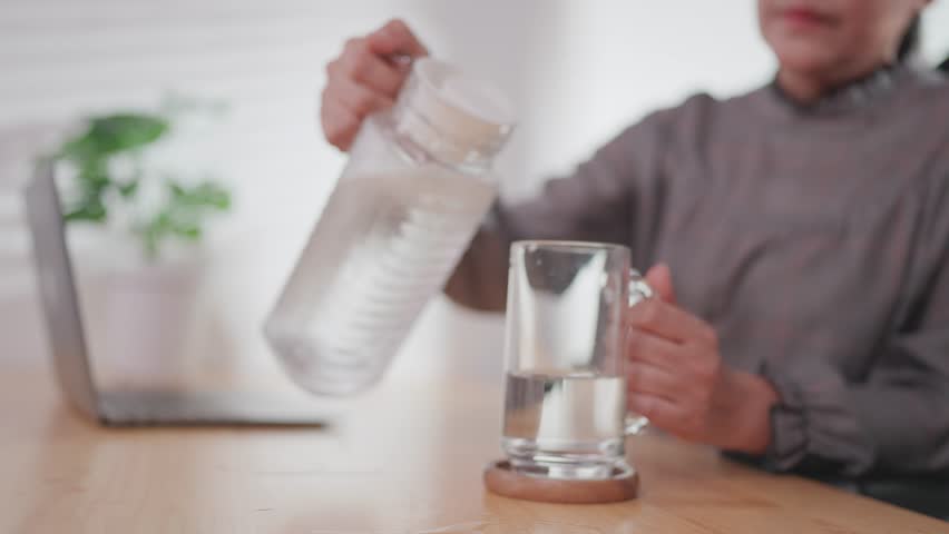 Close-up of woman pouring water to drink during thirst in summer on table in front of laptop	
