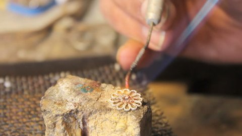 welding a precious stone on a flower shaped jewelry
