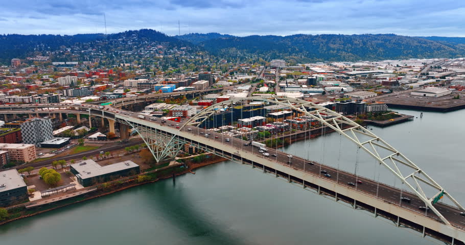 Flying closer to the structure of the Fremont Bridge with multiple transport moving by. Beautiful mountainous panorama of Portland, Oregon, US from top view.