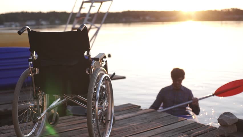 A man with a disability is kayaking against the backdrop of a golden sunset