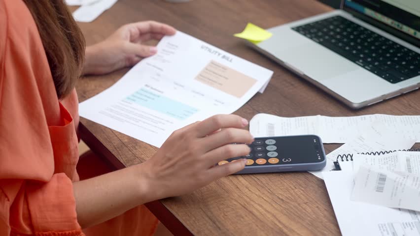 woman, home-bound, settles household utility bills online via her laptop, clutching payment receipts, ensuring timely payments