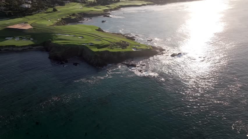 Aerial view of iconic seaside 7th hole at Pebble Beach Golf Links as sunshine reflects off pacific ocean