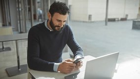 Excited bearded man in office celebrates success with phone and laptop