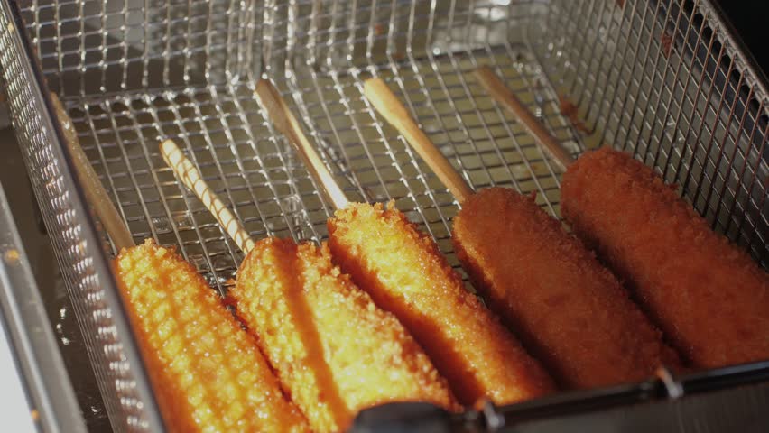 Cooking corn dogs in boiling oil close-up. Traditional asian corndog snacks street food. Fried sausage in breadcrumbs on a stick. Korean Chinese street local market with traditional food. American Royalty-Free Stock Footage #3497252879