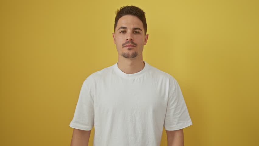 Cheery, young hispanic man in a white t-shirt, standing, looking sanguinely happy. sporting a confident, toothy smile against an isolated yellow cutout, exuding positivity and casual success
